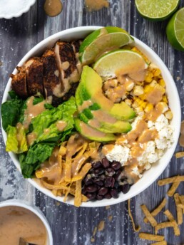 Cajun chicken, romaine lettuce, corn. feta, black beans, dates, tortilla strips, avocado, and limes are added into a bowl and tossed with peanut lime vinaigrette