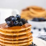 Fluffy Golden Buttermilk Pancakes stacked high, topped with fresh berries and drizzled with sweet maple syrup