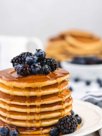 Fluffy Golden Buttermilk Pancakes stacked high, topped with fresh berries and drizzled with sweet maple syrup