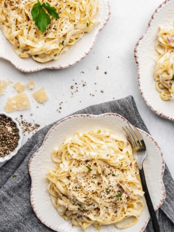 Creamy pasta carbonara is topped with fresh parsley and crispy pancetta