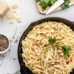 Creamy pasta carbonara is topped with fresh parsley and crispy pancetta in a pan, ready to be served