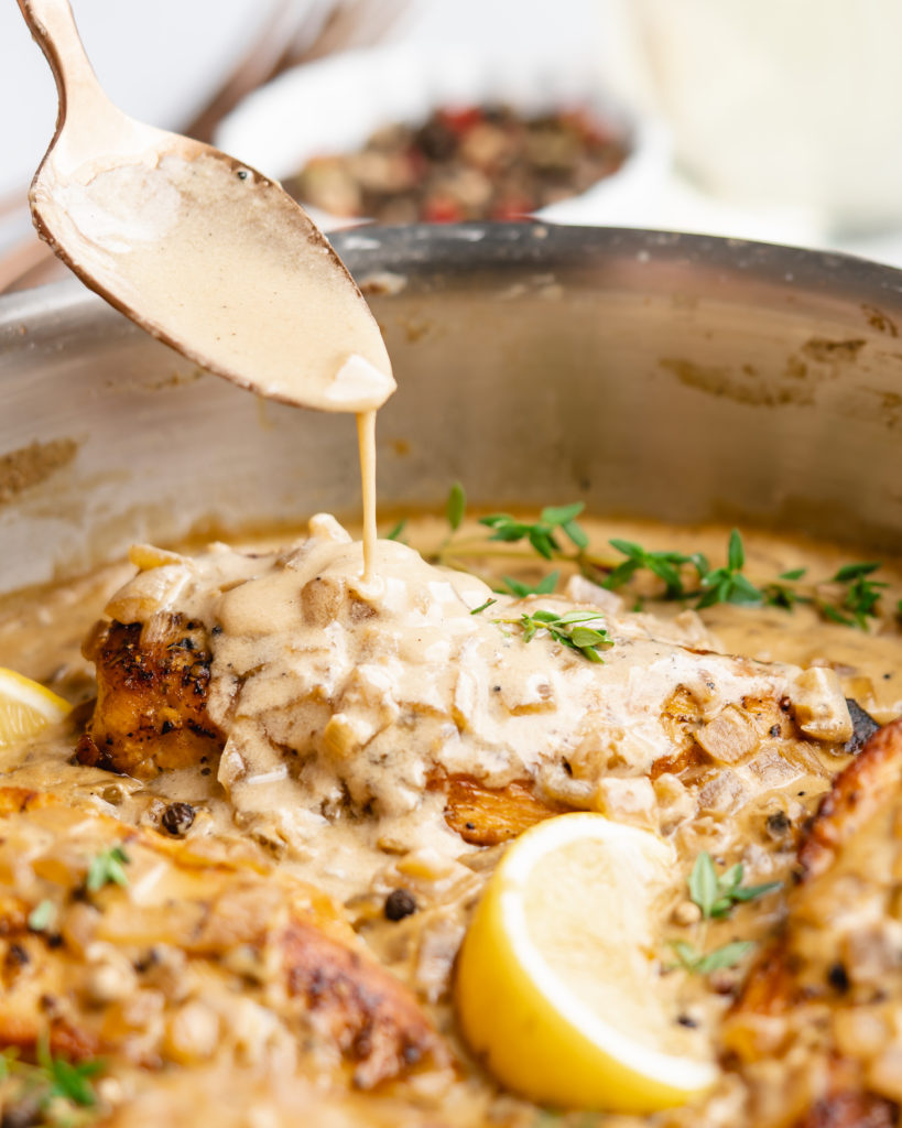 Chicken in pan, topped with white wine cream sauce, spoon drizzling sauce over top