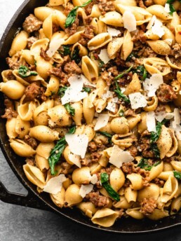 Creamy shell pasta is surrounded by browned crispy sausage, colorful spinach, and delicious pecorino cheese