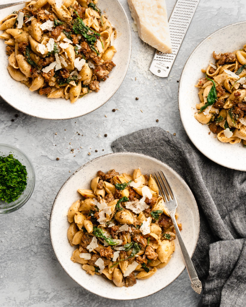 Creamy shell pasta is surrounded by browned crispy sausage, colorful spinach, and delicious pecorino cheese