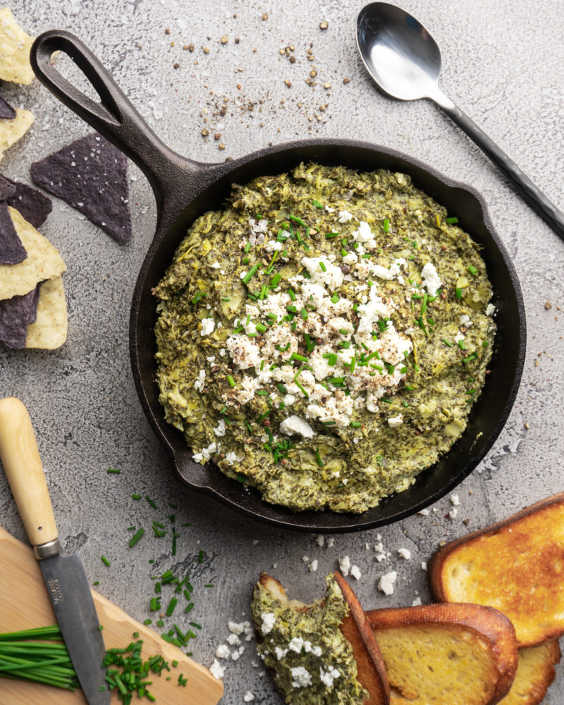 Creamy bright green spinach dip and artichoke dip, topped with feta cheese and chives and served warm