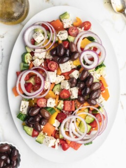 This easy greek salad features peppers, cucumbers, cherry tomatoes, Kalamata olives, feta cheese, red onions, and a homemade dressing