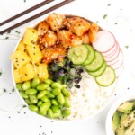 Crispy pieces of chicken covered in a homemade sweet chili sauce are accompanied by mango, cucumber, edamame, radishes, and jasmine rice