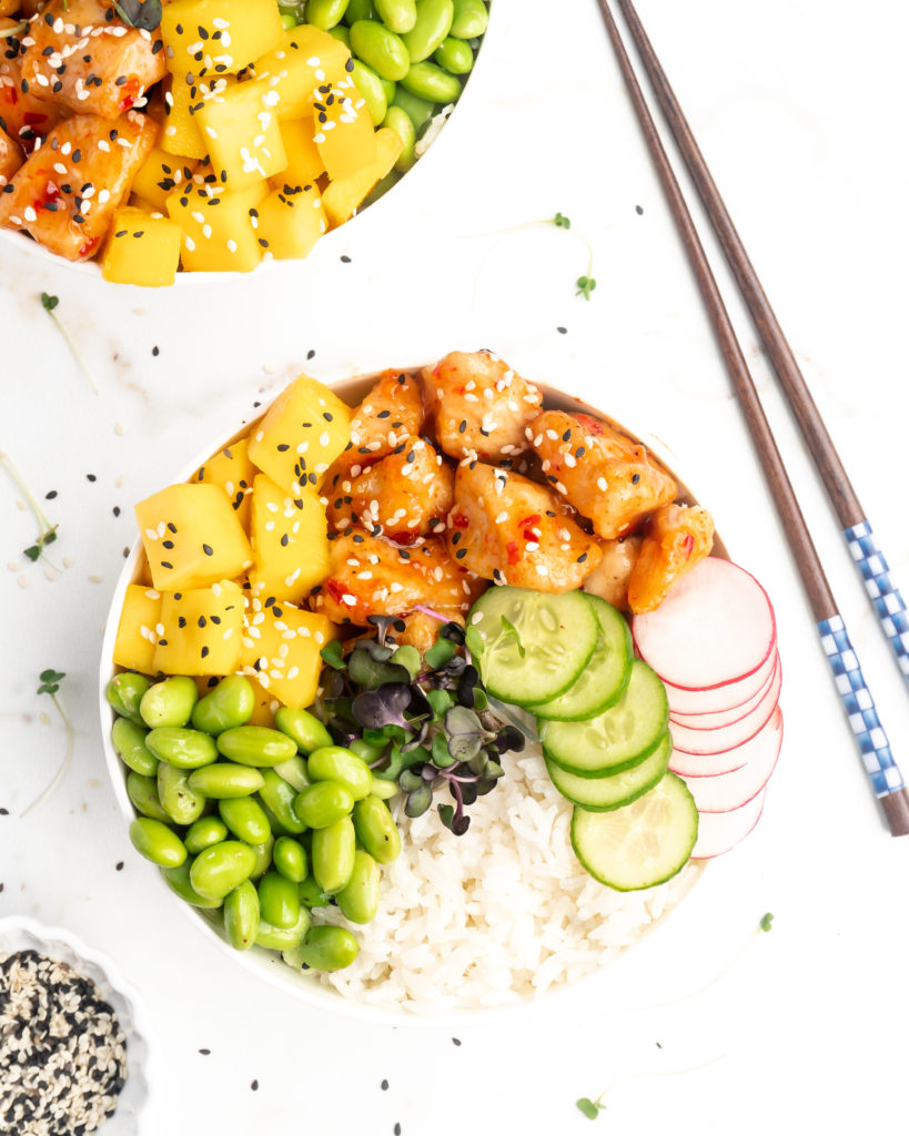 Crispy pieces of chicken covered in a homemade sweet chili sauce are accompanied by mango, cucumber, edamame, radishes, and jasmine rice