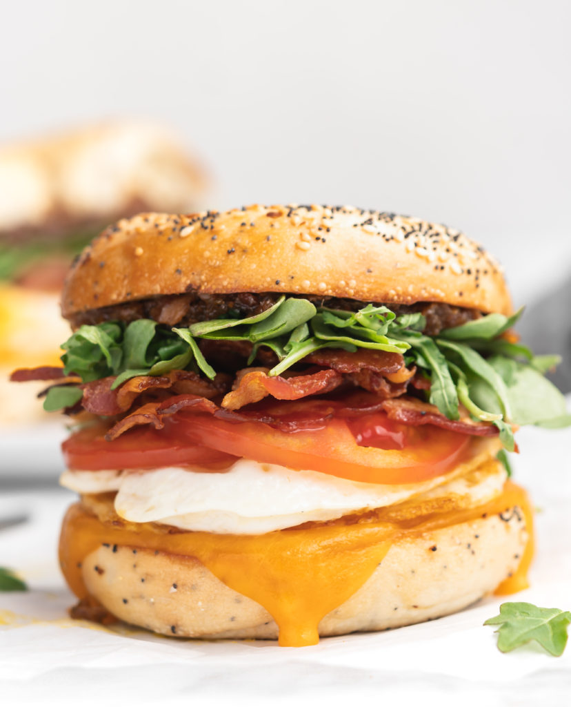 This bagel breakfast sandwich features cheddar, a fried egg, crispy bacon, juicy tomatoes, peppery arugula, sweet apple chutney, and savory bacon jam, all sandwiched between a garlicky everything bagel