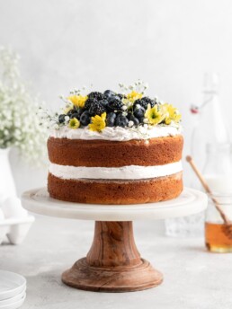 2 layer naked styled chamomile and honey infused cake is decorated with berries and flowers