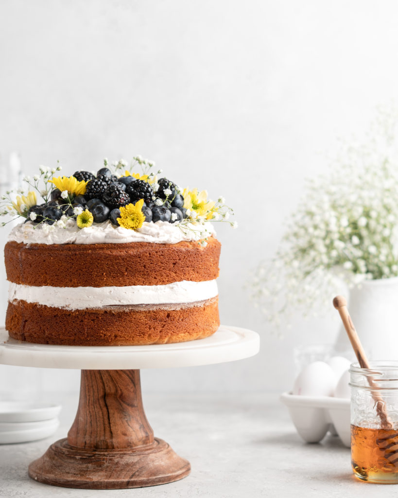 2 layer naked styled chamomile and honey infused cake is decorated with berries and flowers