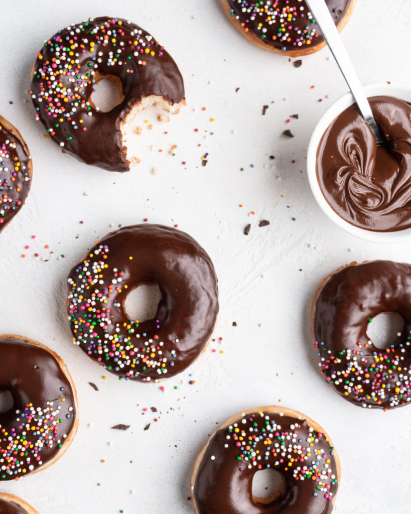 Fluffy golden fried yeast donuts are glazed with a shiny chocolate glaze and colorful round sprinkles