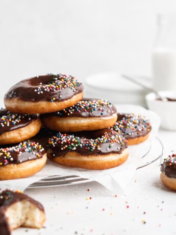 Fluffy golden fried yeast donuts are glazed with a shiny chocolate glaze and colorful round sprinkles