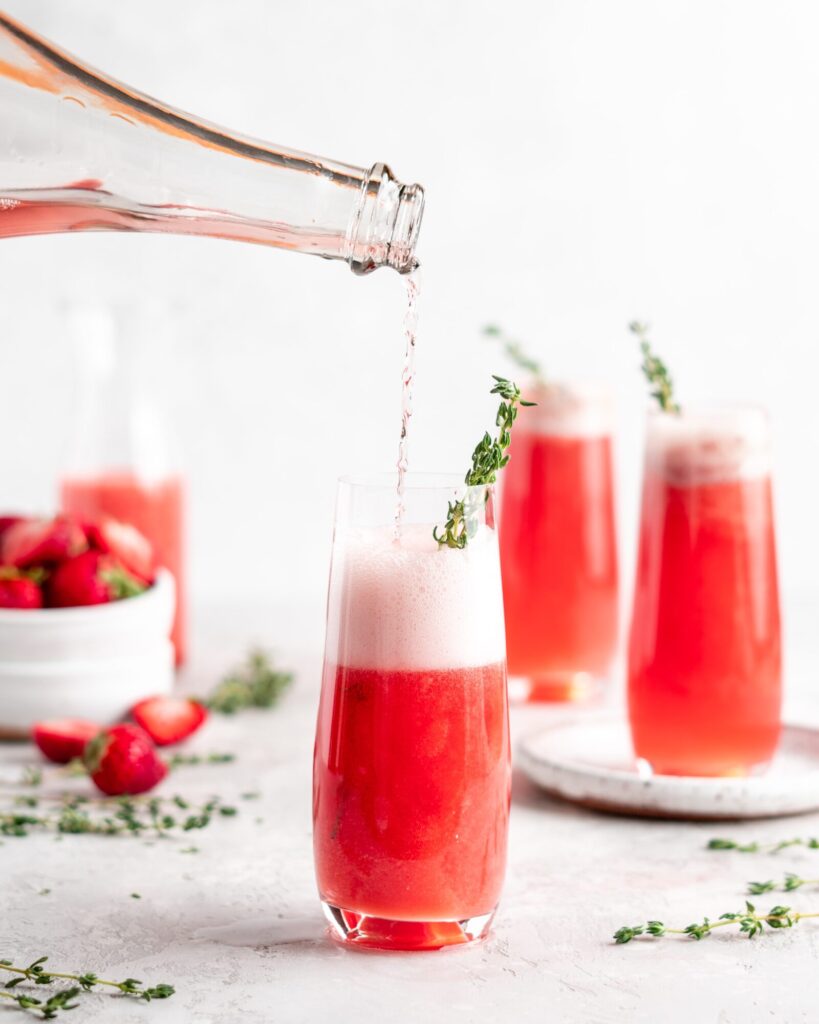 Bright red strawberry guava juice is mixed with sparkling rose wine in stemless champagne glasses to make Strawberry Guava Mimosa