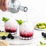 This blackberry rhubarb cocktail features a blackberry rhubarb syrup, soda water, vodka, mint, and lime