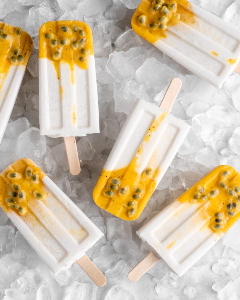 Tropical popsicles featuring mango, passion fruit, and coconut lay on a bed of ice