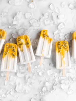 Tropical popsicles featuring mango, passion fruit, and coconut lay on a bed of ice