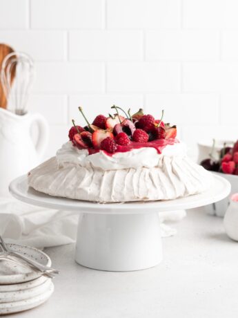 Fluffy and delicious Pavlova is topped with raspberry curd, fresh whipped cream, and loads of summer berries.