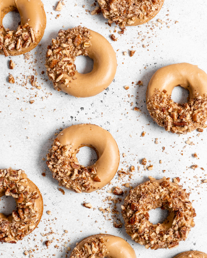 Baked Spiced Brown Sugar Donuts are glazed in a butter maple glaze and garnished with a crushed pecan crust