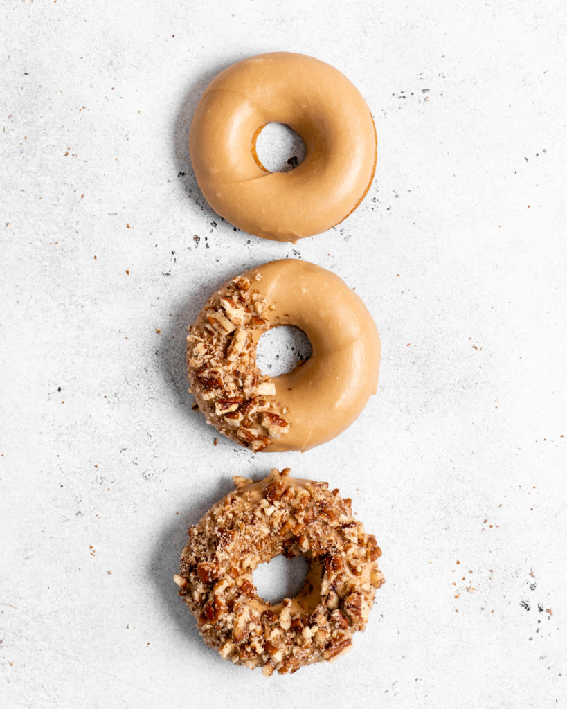 Baked Spiced Brown Sugar Donuts are glazed in a butter maple glaze and garnished with a crushed pecan crust