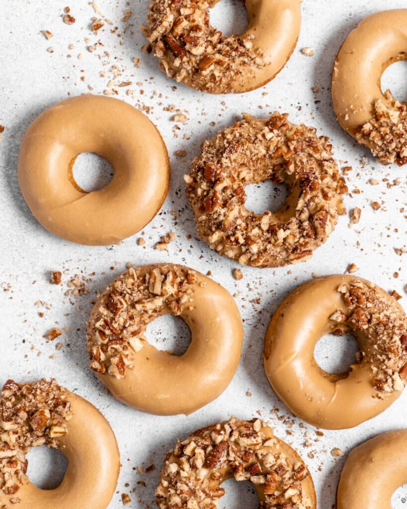 Baked Spiced Brown Sugar Donuts are glazed in a butter maple glaze and garnished with a crushed pecan crust