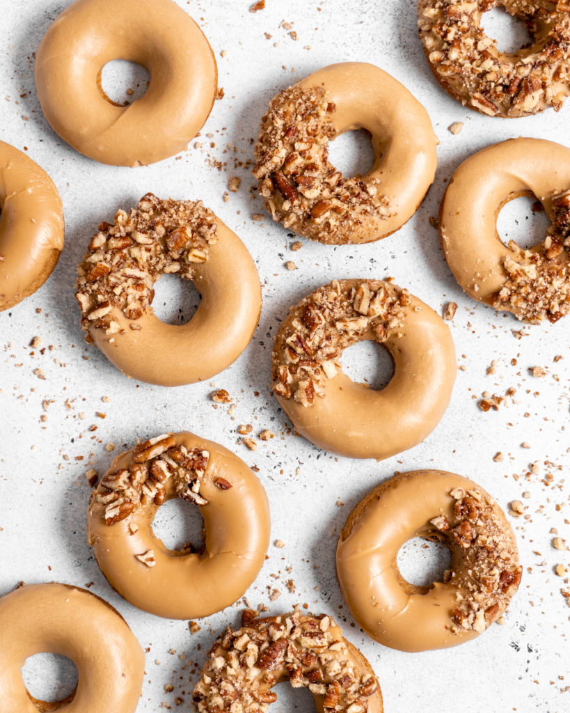 Baked Spiced Brown Sugar Donuts are glazed in a butter maple glaze and garnished with a crushed pecan crust