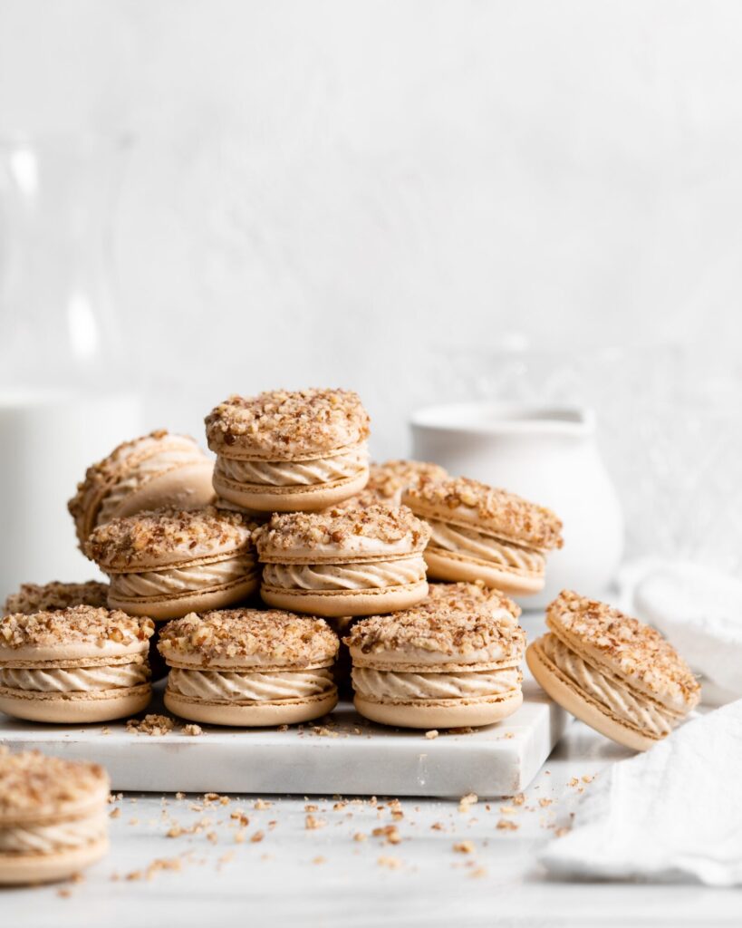 Maple pecan macarons using swiss method, filled with rich maple flavor, the macarons also have a maple buttercream that is speckled with little pecan bits, and a pecan crusted top