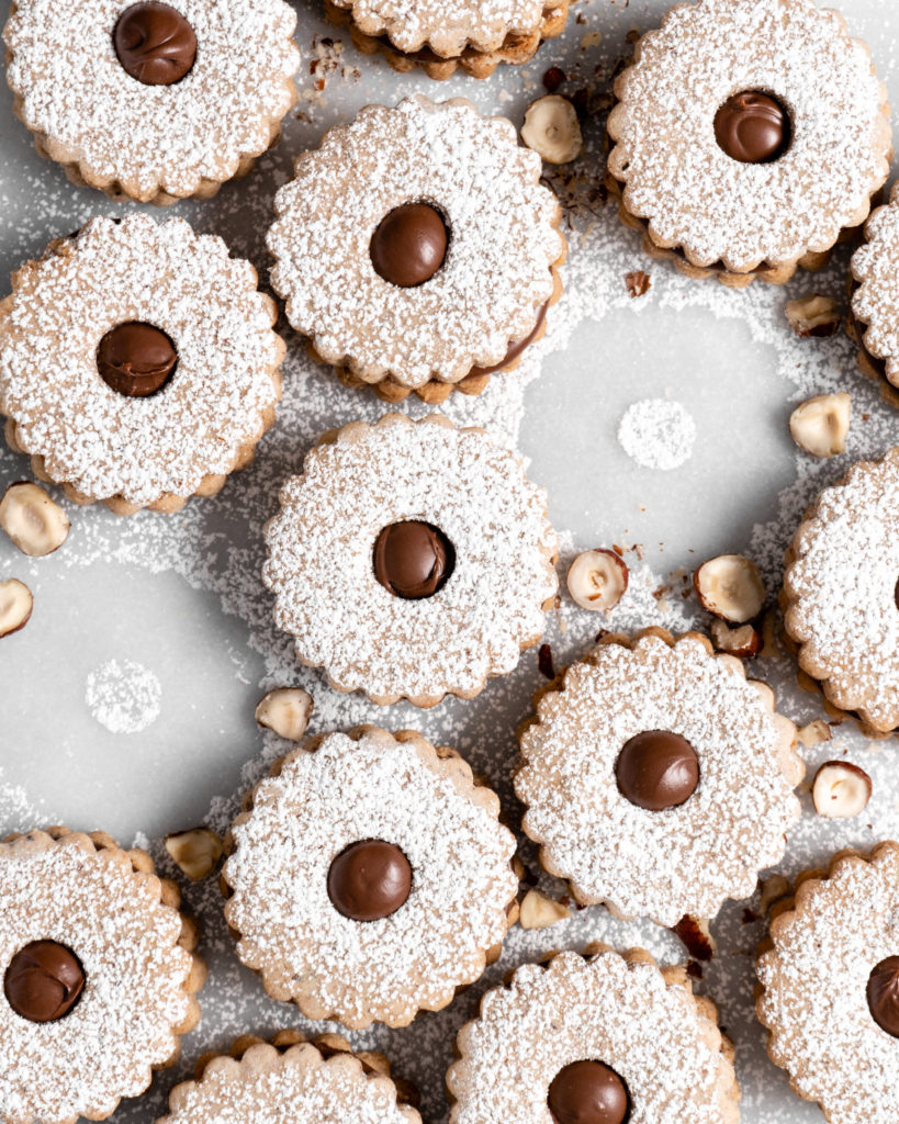 Flower shaped linzer cookies filled with nutella, sandwiched together, and dusted with confectioners sugar