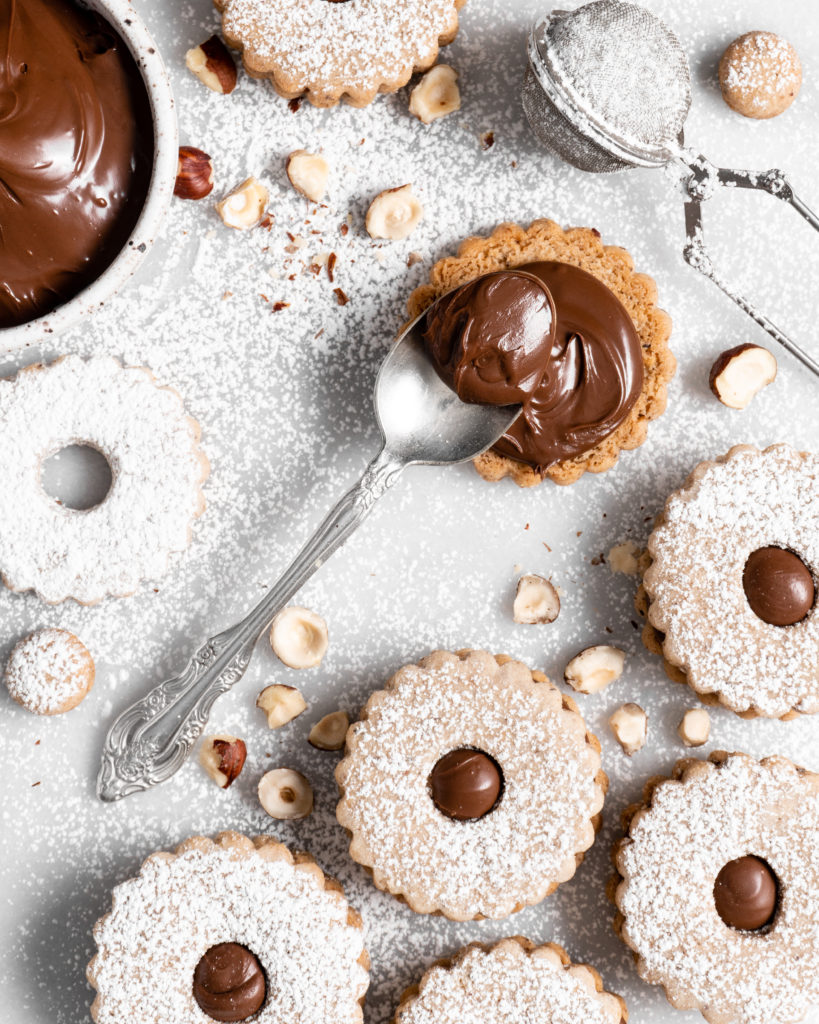 Flower shaped linzer cookies filled with nutella, sandwiched together, and dusted with confectioners sugar