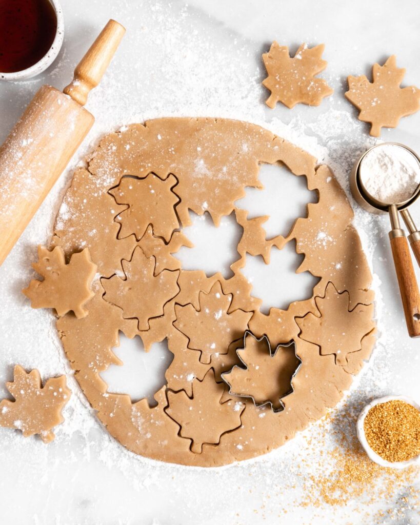 maple sugar cookie rolled out dough with cut out maple leaf cookies