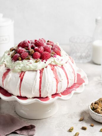 Thick fluffy pavlova topped with whipped pistachio white chocolate ganache and fresh raspberry curd