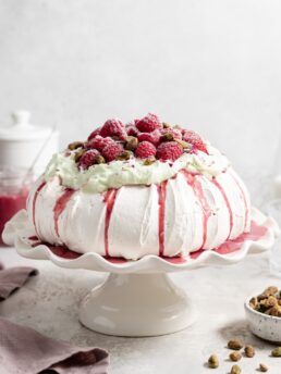 Thick fluffy pavlova topped with whipped pistachio white chocolate ganache and fresh raspberry curd