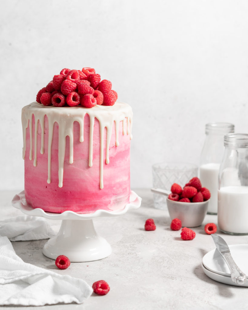 Pink Raspberry Layer Cake with white chocolate drip. Topped with fresh raspberries