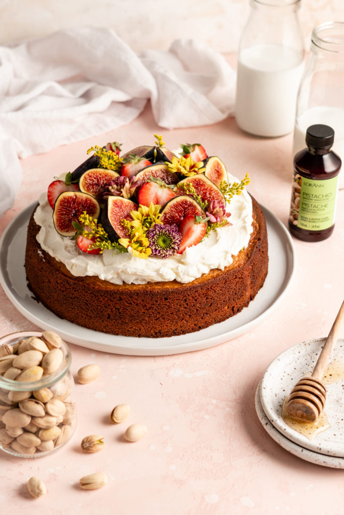 Single layer pistachio cake is topped with creamy honey buttercream and a ton of fresh fruit and flowers