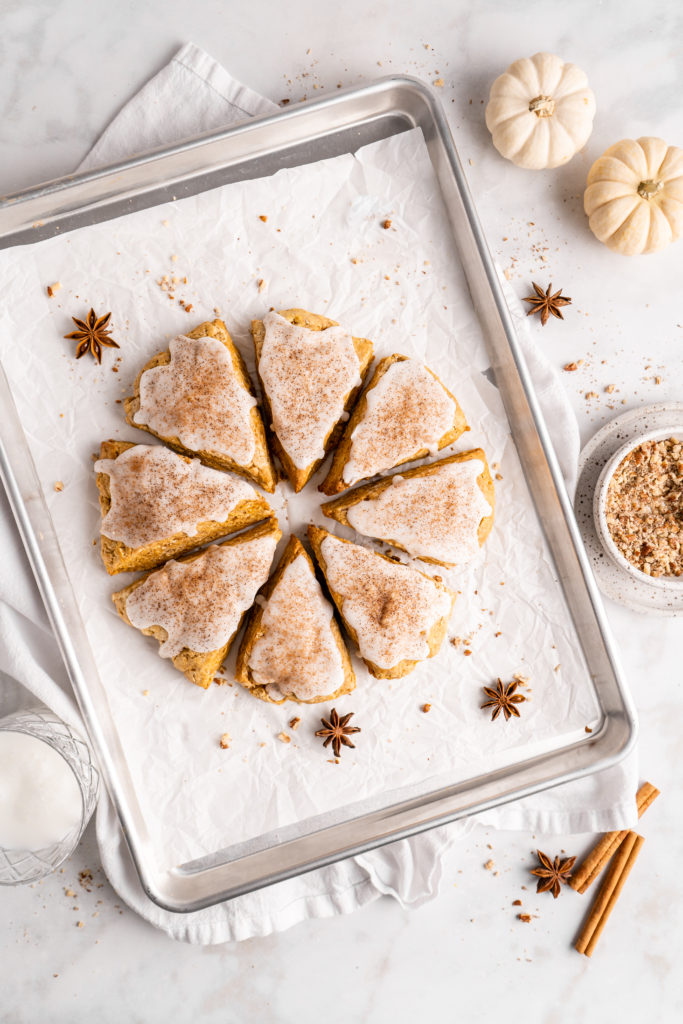 flaky and tender chai pumpkin scones with vanilla glaze, sprinkled with cinnamon and cloves