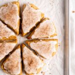 flaky and tender chai pumpkin scones with vanilla glaze, sprinkled with cinnamon and cloves