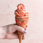 strawberry crunch cheesecake cone being held by hand.