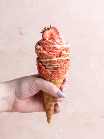 strawberry crunch cheesecake cone being held by hand.