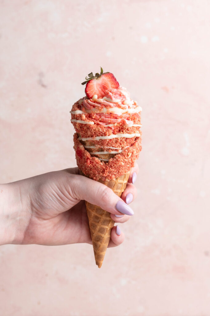 strawberry crunch cheesecake cone being held by hand.